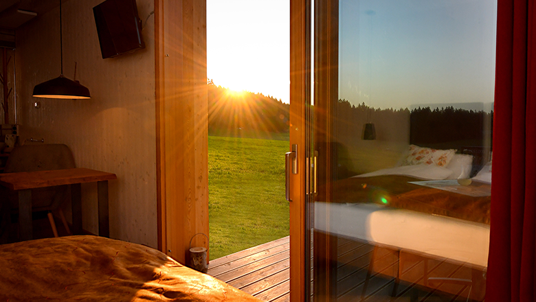 View from a room onto a terrace at sunset, with meadow and forest in the background.