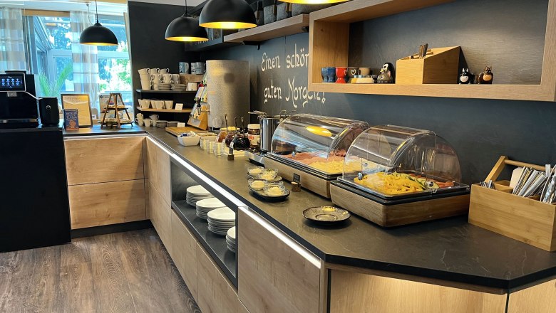 A breakfast buffet with various dishes, crockery and a coffee machine in a modern room.