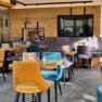 Innenansicht eines modernen Cafés mit bunten Samtstühlen und Holzwänden.