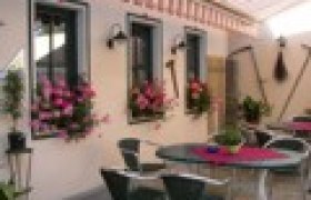 Gem&uuml;tlicher Au&szlig;enbereich eines Gasthauses mit Tischen, St&uuml;hlen und Blumen.