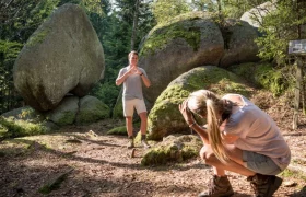 Ein Mann posiert vor einem großen herzförmigen Felsen im Wald, während eine Frau ein Foto von ihm macht.