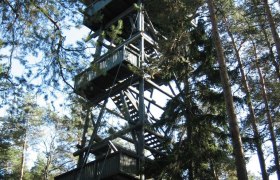 Holzturm im Wald mit mehreren Plattformen und Treppen.