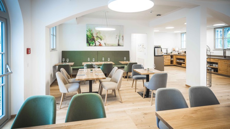 Modernes Restaurant mit Holztischen und gepolsterten Stühlen, helle Beleuchtung und Kunst an der Wand.