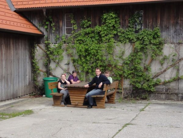 Vier Personen sitzen an einem Holztisch vor einem mit Efeu bewachsenen Gebäude.