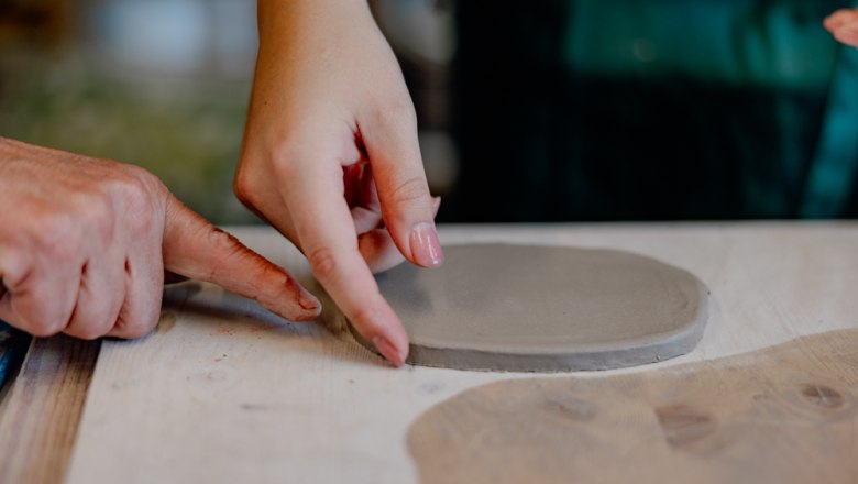 Zwei Hände formen Ton auf einem Tisch.