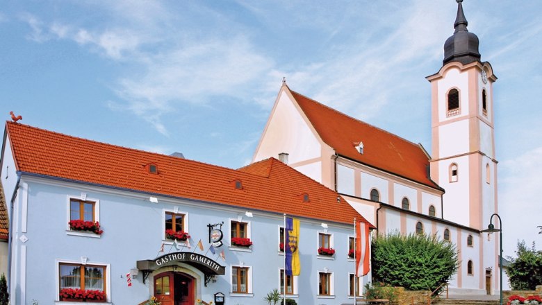 Gamerith Inn, © Gasthaus Gamerith Gasthaus Gamerith next to a church with a tower and red roof.