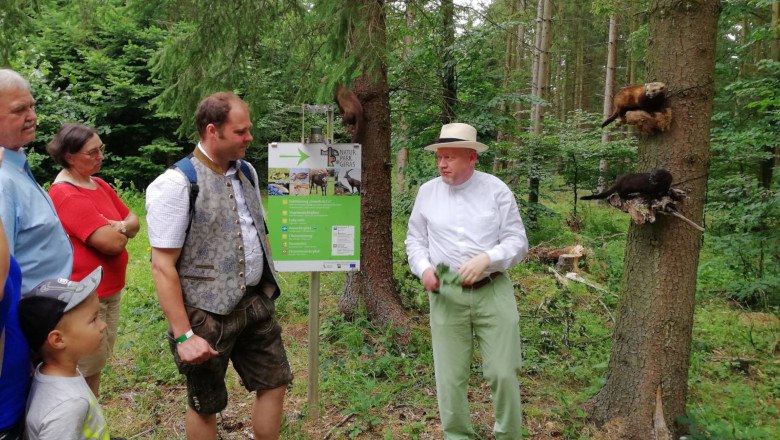 Gruppe von Menschen im Wald, die einem Mann zuhören, der vor einem Schild im Naturpark Geras steht.