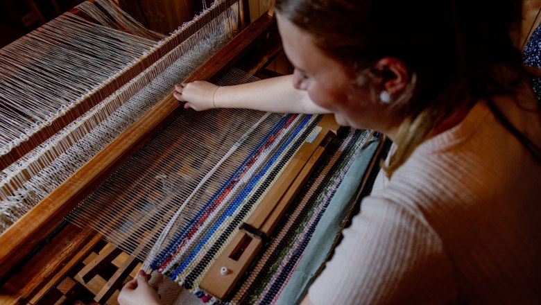 Person webt an einem Webstuhl einen bunten Fleckerlteppich.