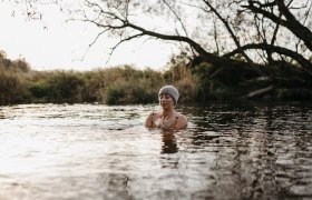 Person mit Mütze badet in einem Fluss bei kühlem Wetter.
