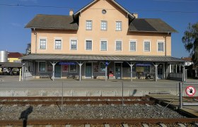 Bahnhof Hadersdorf am Kamp mit Gleisen im Vordergrund und einem gelben Geb&auml;ude im Hintergrund.