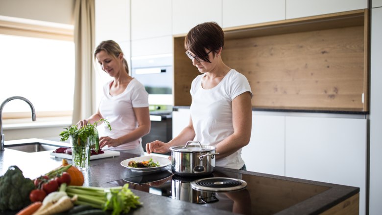 Zwei Frauen kochen in einer modernen Küche mit frischem Gemüse auf der Arbeitsplatte.