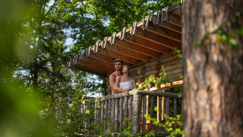 Ein Paar steht auf einem Holz-Balkon in einem Wald, umgeben von Bäumen.