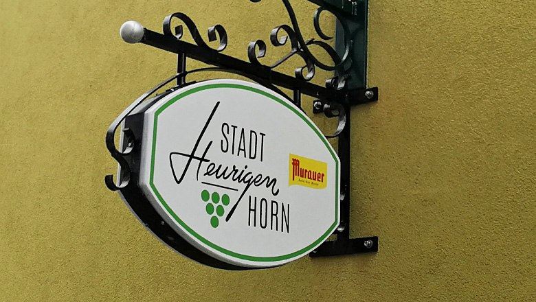 Schild des Stadtheurigen Horn an einer gelben Wand.