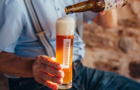 Eine Person schenkt Bier aus einer Flasche in ein Glas mit der Aufschrift 'HaselBräu'.