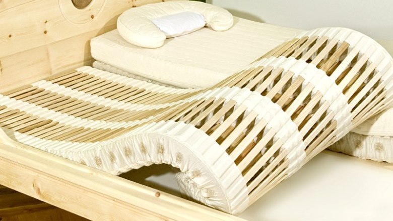 A bed with a wave-shaped slatted frame and light-colored wooden frame.