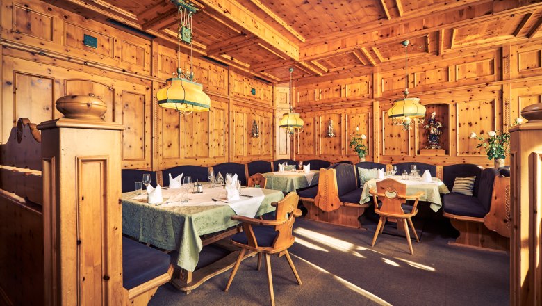 Cozy Zirbenstube with wooden walls, tables and chairs, decorated with lamps and plants.
