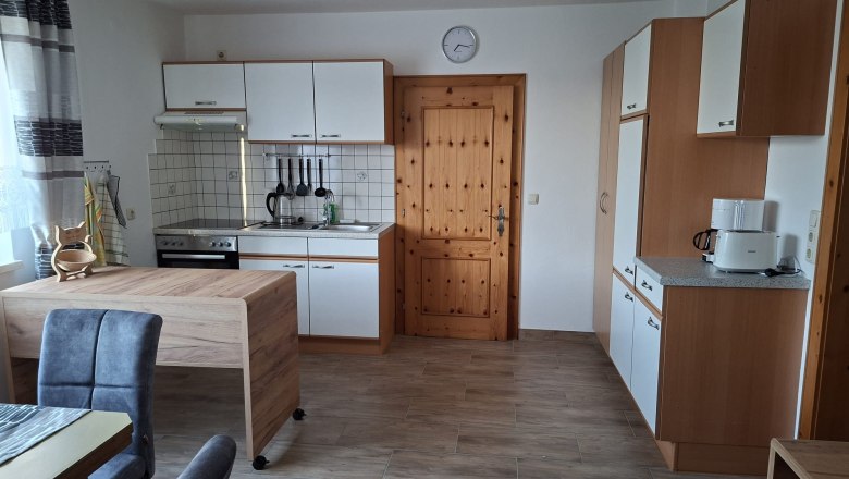 Moderne K&uuml;che mit Holz- und wei&szlig;en Elementen, Esstisch, St&uuml;hlen und K&uuml;chenger&auml;ten.