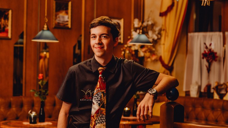 Junger Mann in einem Restaurant mit Krawatte und Hemd, lächelnd.