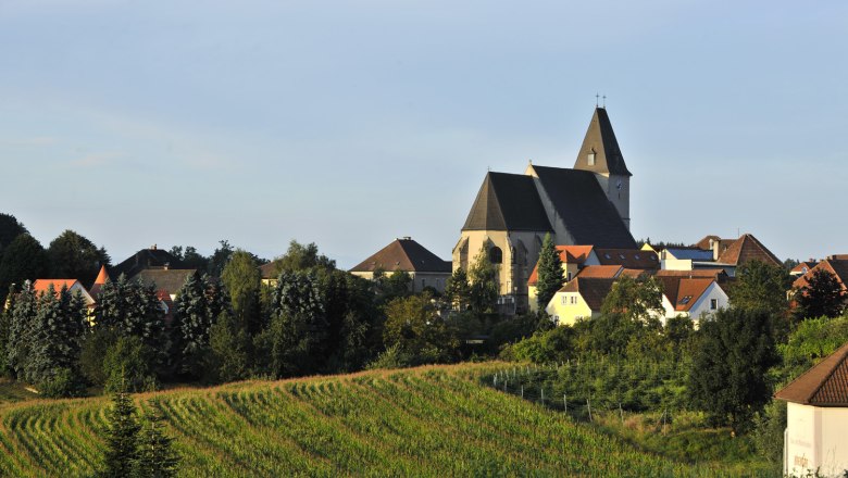 Landschaft mit Kirche und Dorf im Hintergrund, umgeben von Feldern und B&auml;umen.