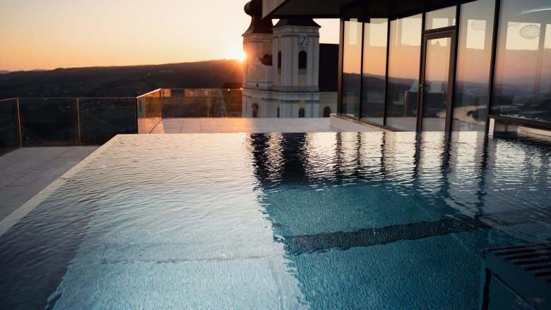 Infinitypool bei Sonnenuntergang mit Blick auf ein Gebäude und die Landschaft.