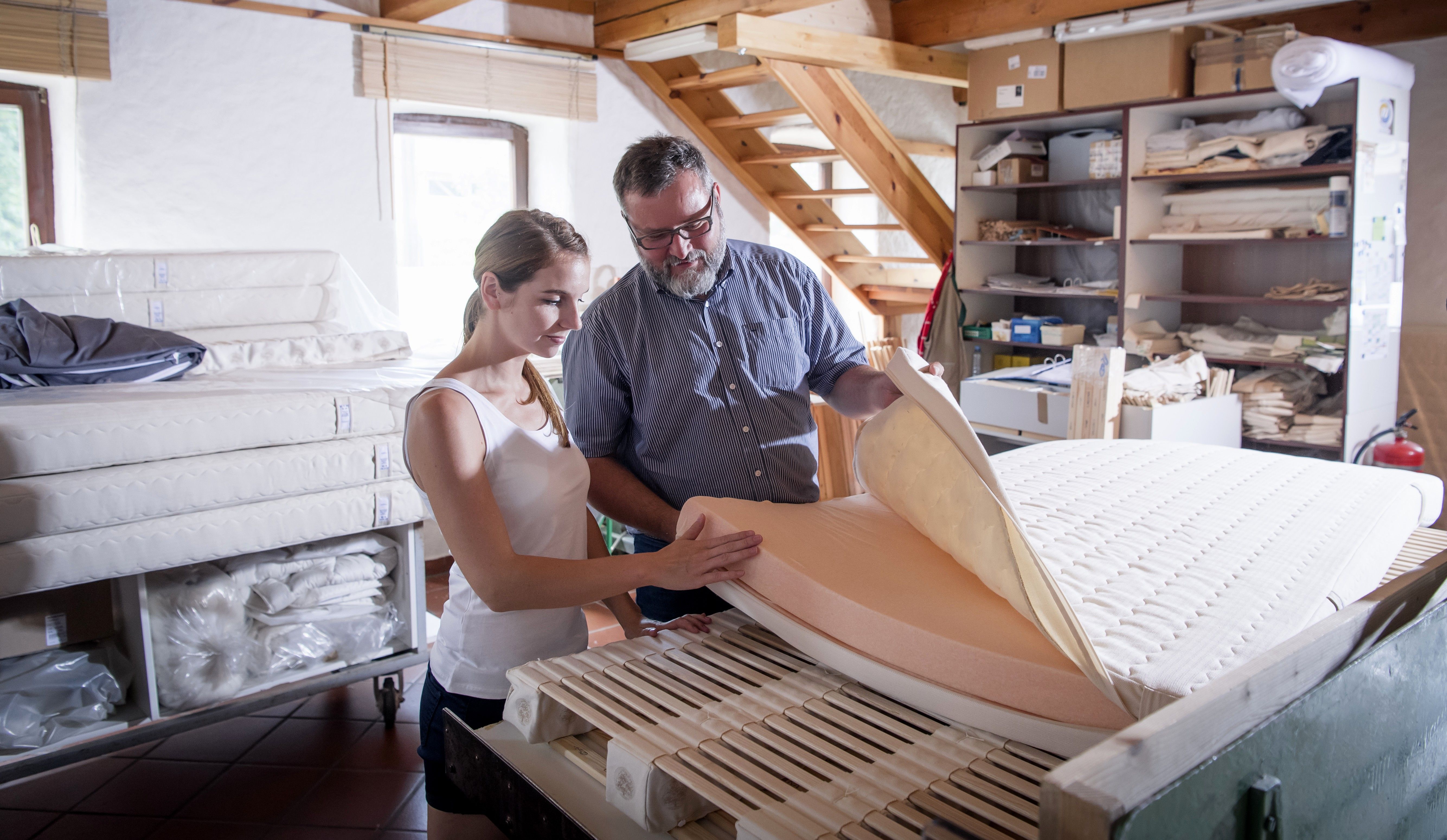 Zwei Personen in einer Werkstatt, die eine Matratze inspizieren.