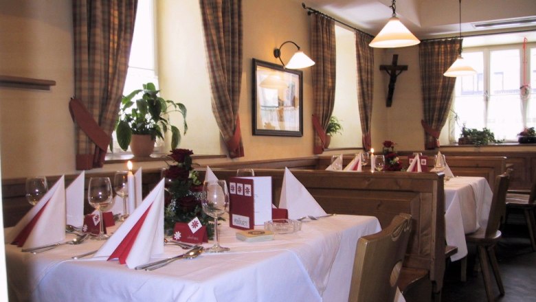 Gemütliches Restaurant mit gedeckten Tischen, Holzmöbeln und karierten Vorhängen.