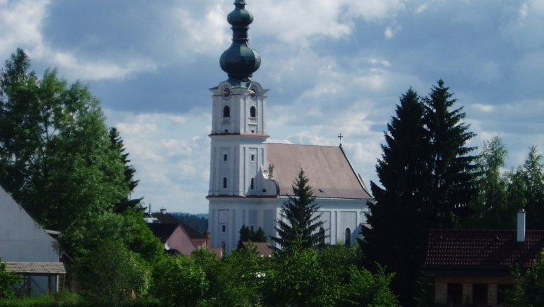 Kirche in Kirchberg am Walde mit Teich im Vordergrund und bewölktem Himmel.