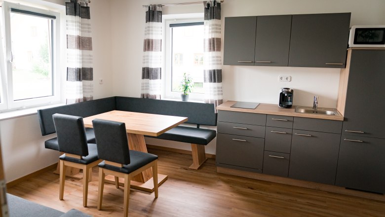 Moderne Küche mit grauen Schränken, Holztisch und Eckbank.