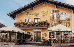 Ein traditionelles Gasthaus mit Balkon und Wandgemälde, umgeben von Sonnenschirmen und Pflanzen.