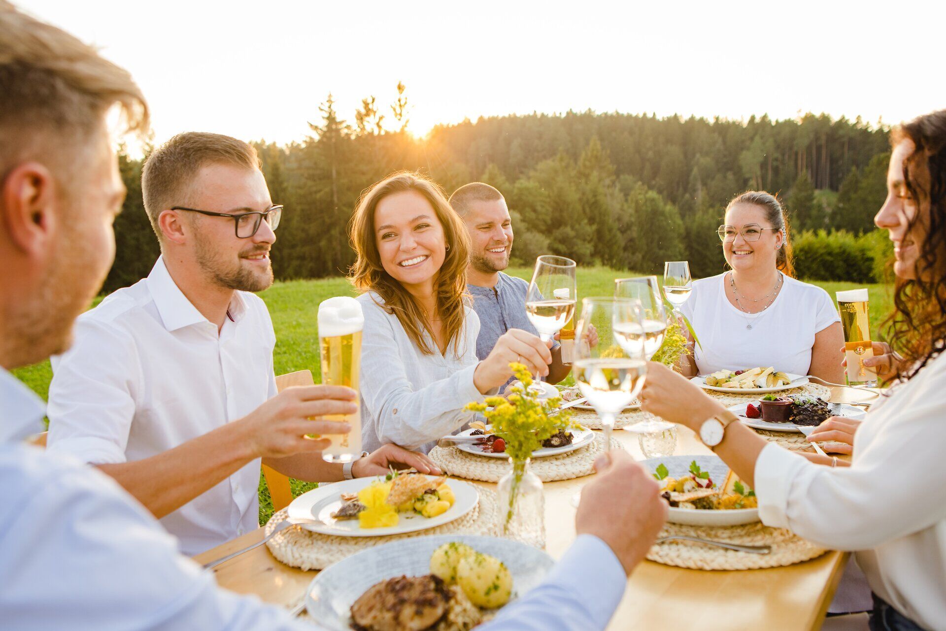 In der warmen Abendsonne versammeln sich Freunde an einem festlich gedeckten Tisch, um die köstlichen Waldviertler Spezialitäten zu genießen. Die fröhlichen Anstoße mit Gläsern voller erfrischender Getränke schaffen eine einladende Atmosphäre, die zum Verweilen einlädt. Umgeben von der malerischen Natur des Waldviertels wird jeder Bissen zu einem unvergesslichen Erlebnis.