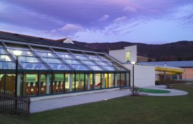 Au&szlig;enansicht des Hallenbads Yspertal bei D&auml;mmerung mit Glasfassade und Rutsche.