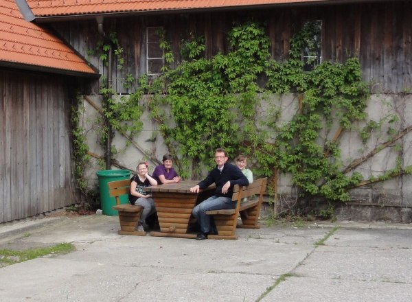Vier Personen sitzen an einem Holztisch vor einem mit Efeu bewachsenen Gebäude.