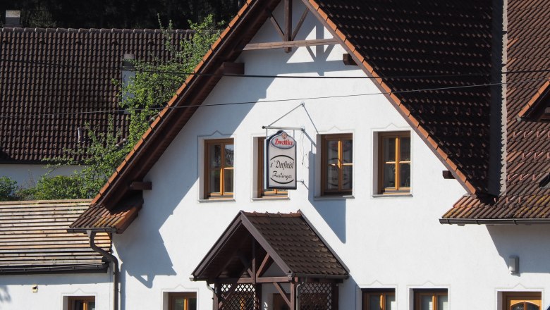 Ein traditionelles Gebäude mit weißen Wänden und braunen Dachziegeln. Ein Schild mit der Aufschrift 'Zwettler Dorfwirt Zeilinger' hängt an der Fassade.