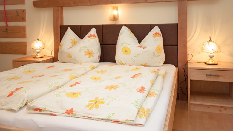 Gemütliches Schlafzimmer mit Doppelbett, Blumenbettwäsche und Nachttischlampen.