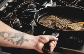 Person brät Fischstücke in einer Pfanne auf einem Herd.