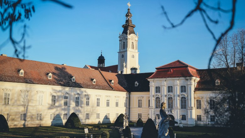 Barockes Klostergebäude mit Turm und Garten im Vordergrund.