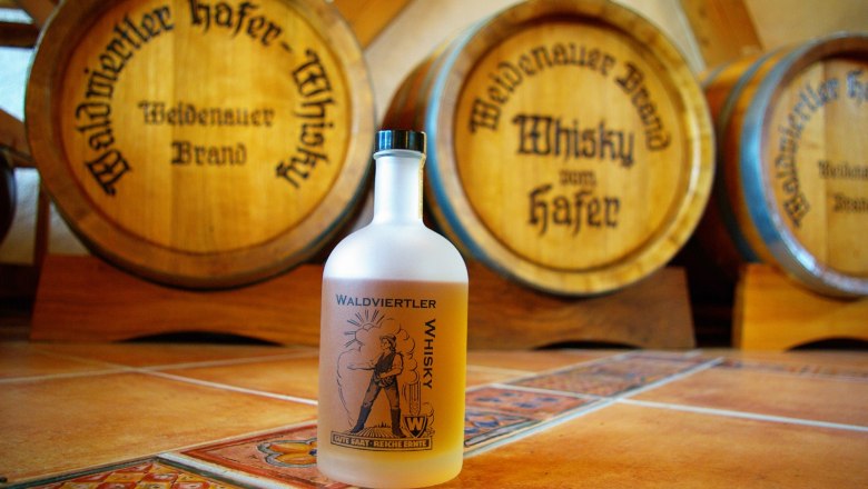 Eine Flasche Waldviertler Whisky vor Holzfässern der Destillerie Weidenauer.