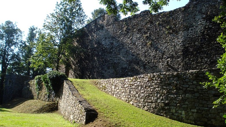 Alte Stadtmauer mit Grünfläche und Bäumen im Sonnenlicht.