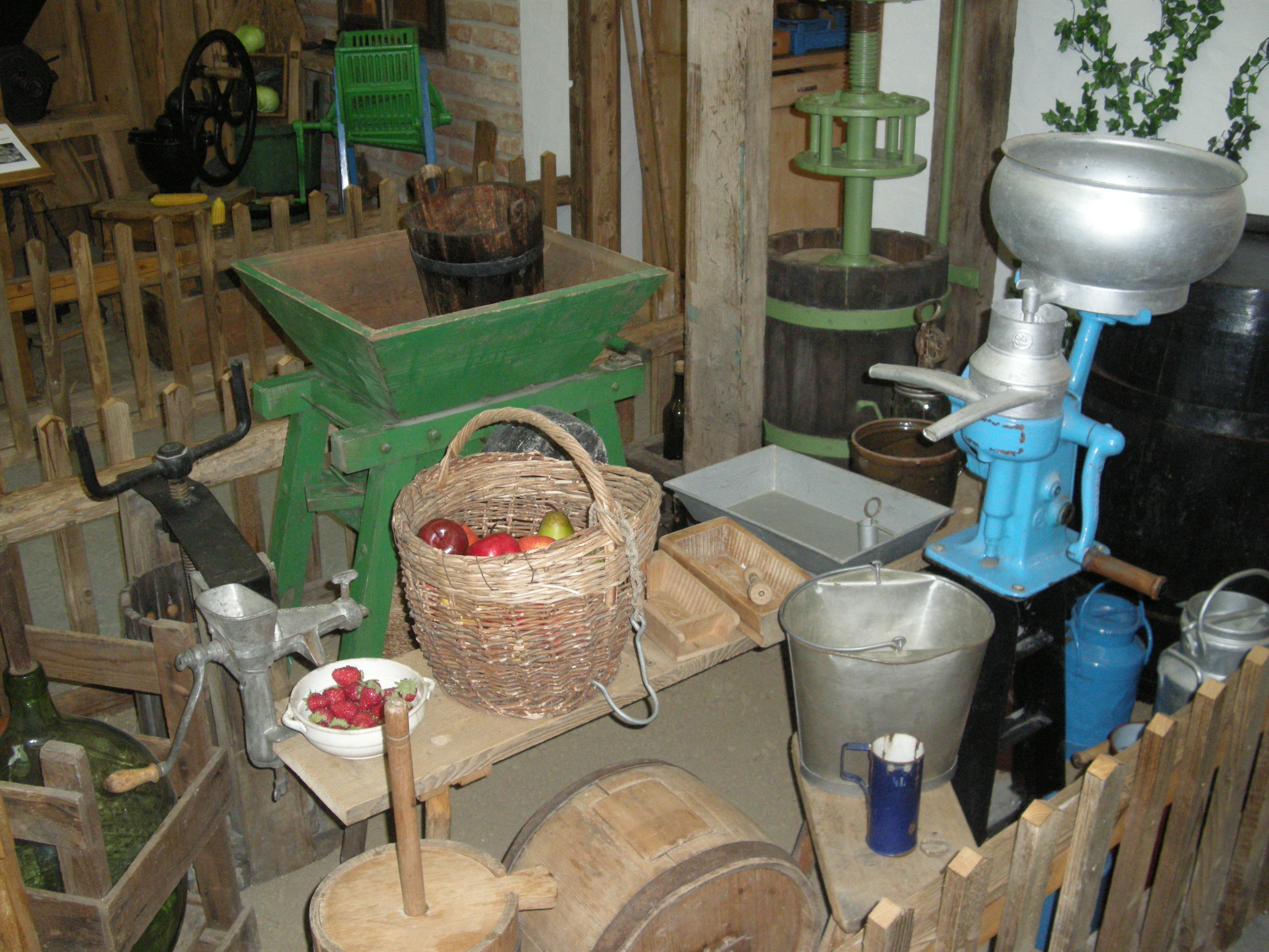 Alte landwirtschaftliche Geräte und ein Korb mit Obst in einem Museum.