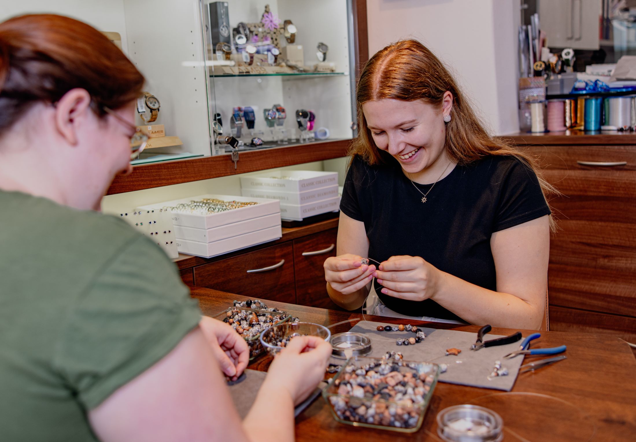 Zwei Frauen fertigen Schmuck aus Granitsteinen an einem Tisch.