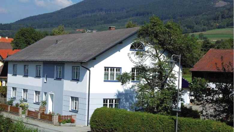 A large, two-storey, white and blue house with a garden and mountain landscape in the background.