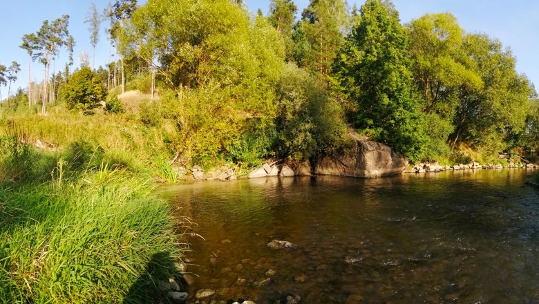 Flusslandschaft mit Bäumen und Felsen am Ufer.