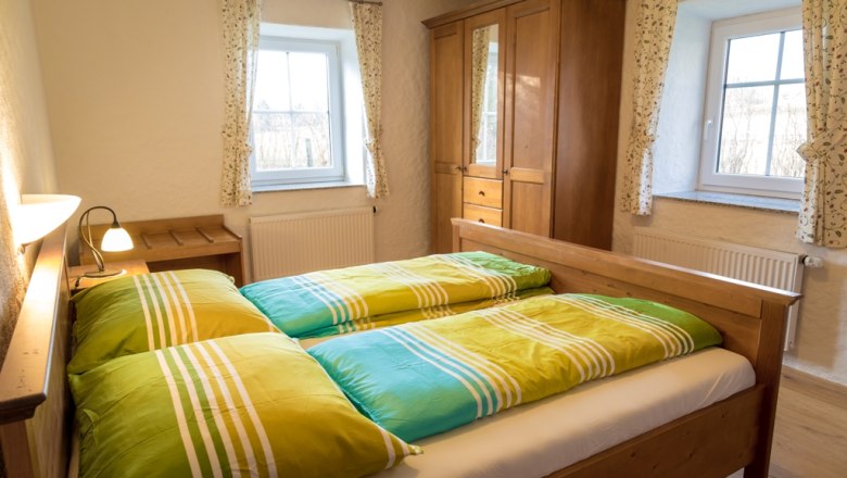 Gem&uuml;tliches Schlafzimmer mit Holzm&ouml;beln und bunten Bettbez&uuml;gen.