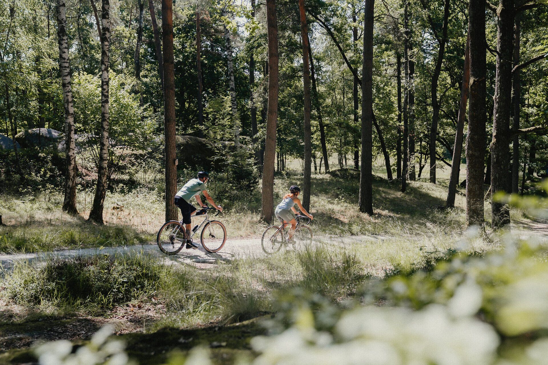 Zwei Personen, umgeben von Wald und Steinen, die mit ihren Rädern durch die Natur fahren