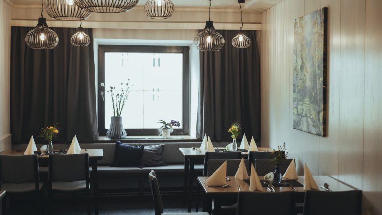 Modern eingerichtetes Gastzimmer mit stilvollen Lampen, gedeckten Tischen und einem großen Fenster.