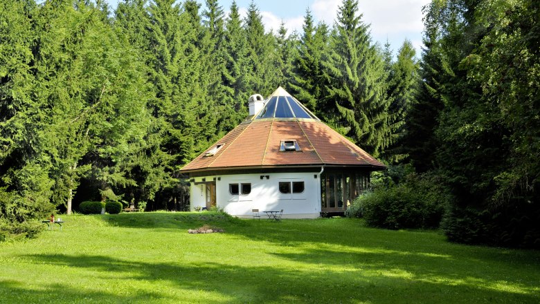 Ein rundes Haus mit Pyramiden-Dach inmitten eines Waldes.