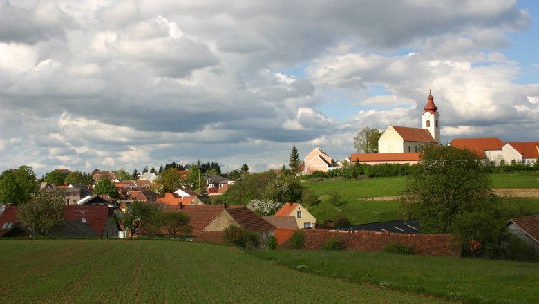 Landschaft mit Dorf und Kirche unter bewölktem Himmel.