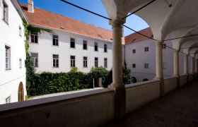 Innenhof eines historischen Gebäudes mit Arkadengang und Efeu bewachsenen Wänden.