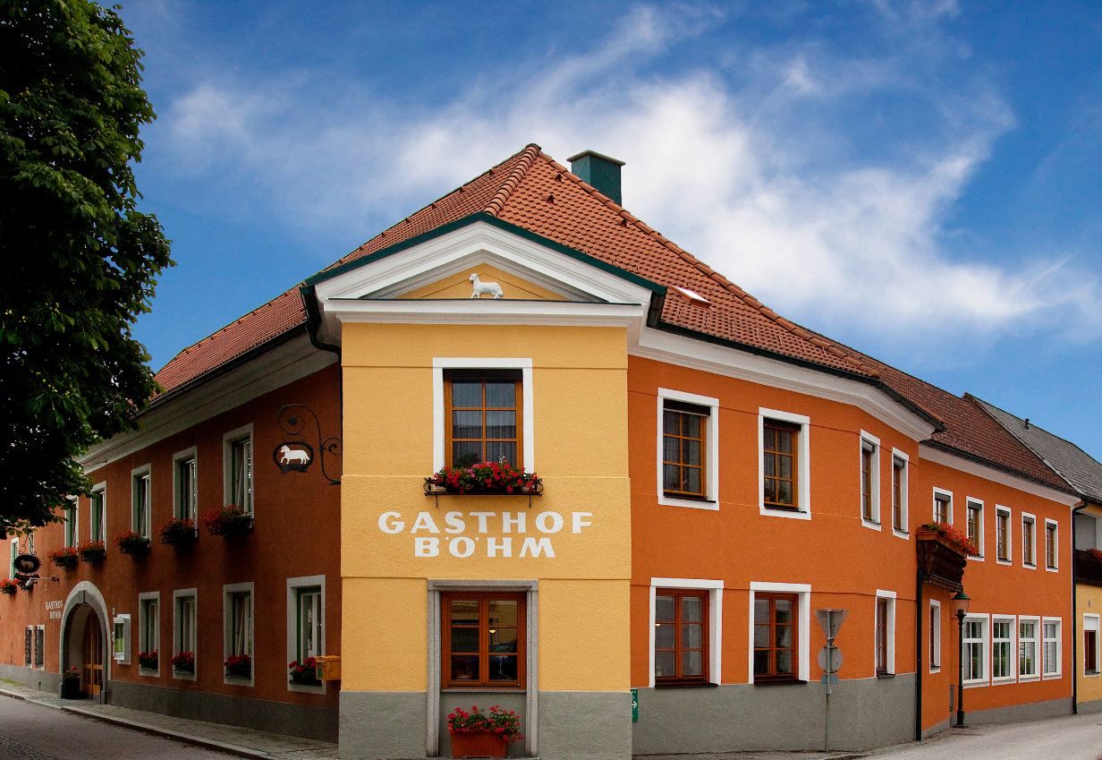 Ein traditionelles Gasthaus mit orange-gelber Fassade und roten Dachziegeln unter blauem Himmel.