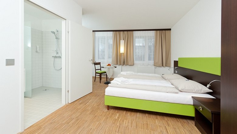 Modernes Hotelzimmer mit Doppelbett, Holzboden und angrenzendem Badezimmer.